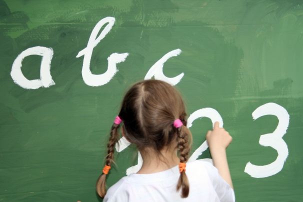 Grundschülerin steht vor einer Tafel und schreibt das ABC